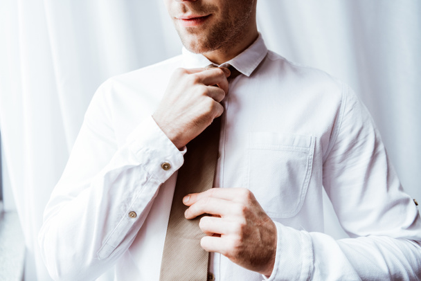 partial view of handsome businessman in white shirt tying neck tie  - Foto, imagen