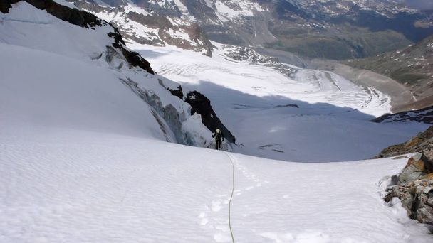 montanhista saindo de uma íngreme face norte nos Alpes Suíços e caminhando até uma geleira para o cume de Piz Cambrena na cordilheira Bernina
 - Foto, Imagem