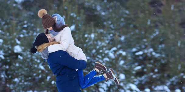 Μερική άποψη του ο άνθρωπος που μεταφέρουν ευτυχισμένη κοπέλα στέκεται στο χιονισμένο όμορφο δάσος βλέπουν ο ένας τον άλλον με αγάπη - Φωτογραφία, εικόνα
