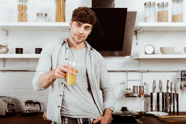 selective focus of young man drinking orange juice on breakfast in kitchen at home - Foto, Bild