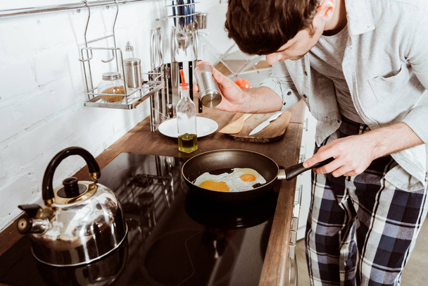 vue partielle du jeune homme cuisinant des œufs brouillés sur une poêle dans la cuisine
  - Photo, image