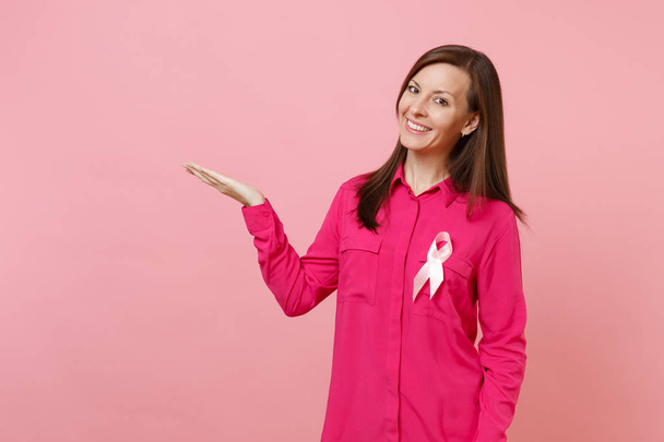 Kobieta w różowe ubrania z różowej wstążki jedwabne symbol na białym tle na tle pastelowe ściany, studio portret. Medycznych opieki zdrowotnej onkologii ginekologicznej, koncepcja świadomości raka piersi. Makieta do miejsca kopiowania - Zdjęcie, obraz
