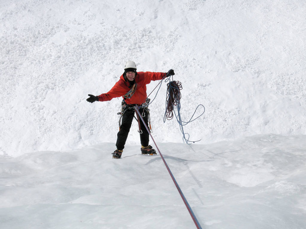 male mountain ice climber rapelling off a steep and long frozen waterfall in the Swiss Alps in deep winter not happy with problems he has with the climbing ropes - Photo, Image