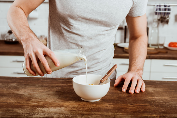 обрезанный образ человека, наливающего молоко в миску с кукурузными хлопьями на кухне дома
 - Фото, изображение