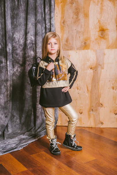 Little cute girl with blond hair in fashionable leggings, with gold and sequins, with a backpack - Foto, Imagen