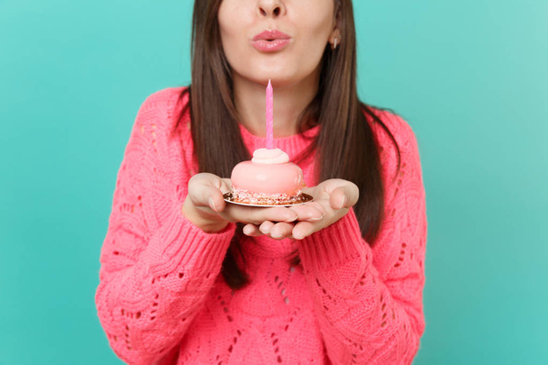 Oříznutý obraz mladé ženy v pletený růžový svetr sfoukl svíčku na dort v rukou izolované na modré tyrkysové zdi pozadí studiový portrét. Koncept životního stylu lidí. Vysmívat se kopie prostor - Fotografie, Obrázek