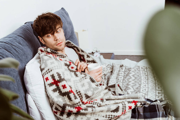 hasta adam yatakta evde çay ile oturup battaniyeye sarılmış seçici odak  - Fotoğraf, Görsel