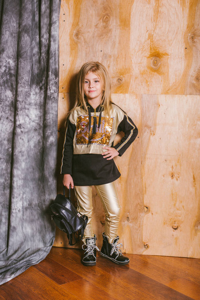 Little cute girl with blond hair in fashionable leggings, with gold and sequins, with a backpack - Fotoğraf, Görsel