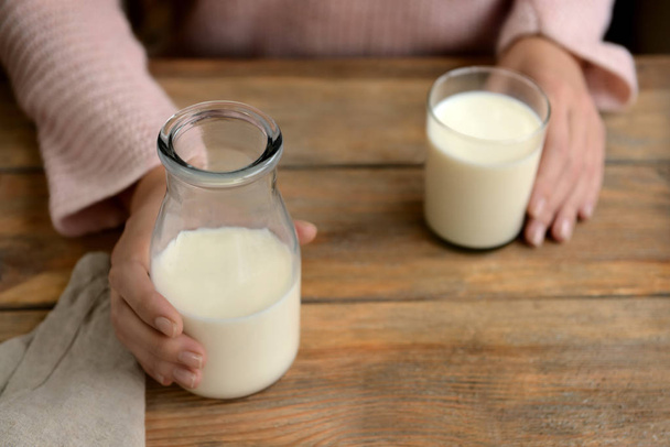 Nainen pullon ja lasin tuoretta maitoa puupöydässä
 - Valokuva, kuva