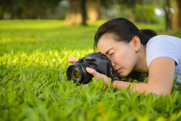 屋外の芝生の上にプロのカメラで写真を取る若い女性写真家 - 写真・画像