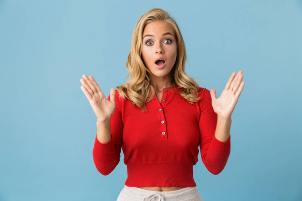 Portrait of excited blond woman 20s wearing red shirt raising hands up isolated over blue background in studio - Foto, immagini