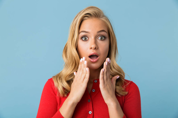 Portrait of excited blond woman 20s wearing red shirt expressing surprise with open mouth isolated over blue background in studio - Foto, imagen
