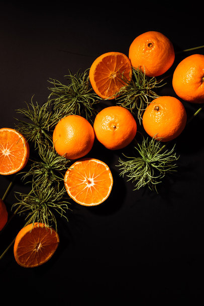 top view of fresh tangerines and green plants arranged on black tabletop - Foto, Imagen