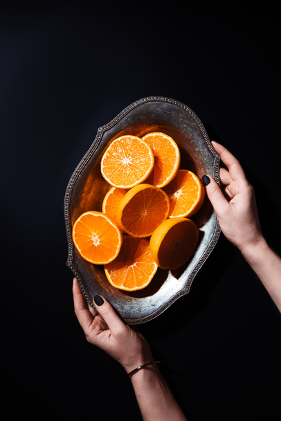 cropped shot of woman holding metal bowl with cut tangerines on black background - Foto, Bild