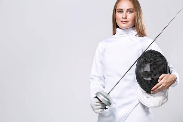 Portrait of Young woman fencer wearing mask and white fencing costume and holding the sword in front of her. Isolated on White Background. - Фото, зображення