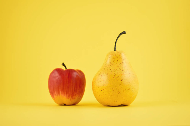 Pear and apple decoration stock images. Yellow pear and red apple on a yellow background. Fruit home decor. Plastic decorative fruit - Foto, Bild