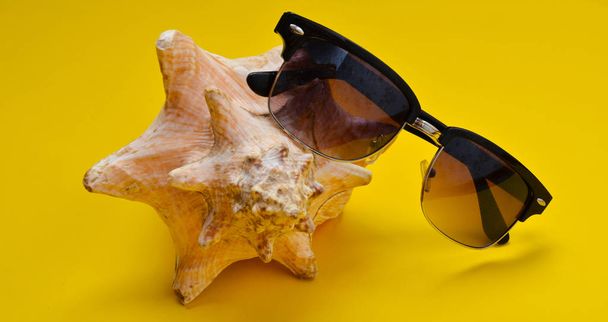 Un grande guscio di mussola e occhiali da sole su uno sfondo giallo. Il concetto di relax in spiaggia
. - Foto, immagini