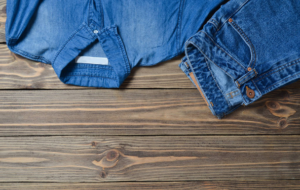 Джинсы брюки и джинсовая рубашка на деревянной поверхности. Вид сверху
. - Фото, изображение