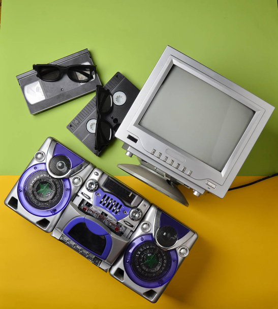 Ретро медиа технологии. Развлечения 80-х. Черно-белый ламповый телевизор, магнитофон, видеокассета, 3D очки на зеленом и желтом фоне. Вид сверху. Плоский лежал
. - Фото, изображение