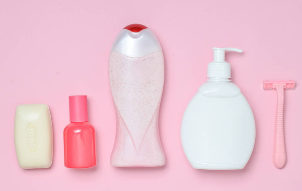 A bottle of fragrant perfume, lotion, shampoo, soap, razor. Products for the care of body, hair and personal hygiene on a pink pastel background.  Top view. Trend of minimalism. Flat lay. - Fotó, kép