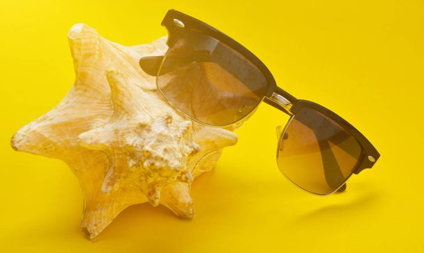 Una gran concha de muselina y gafas de sol sobre un fondo amarillo. El concepto de relajarse en la playa
. - Foto, Imagen