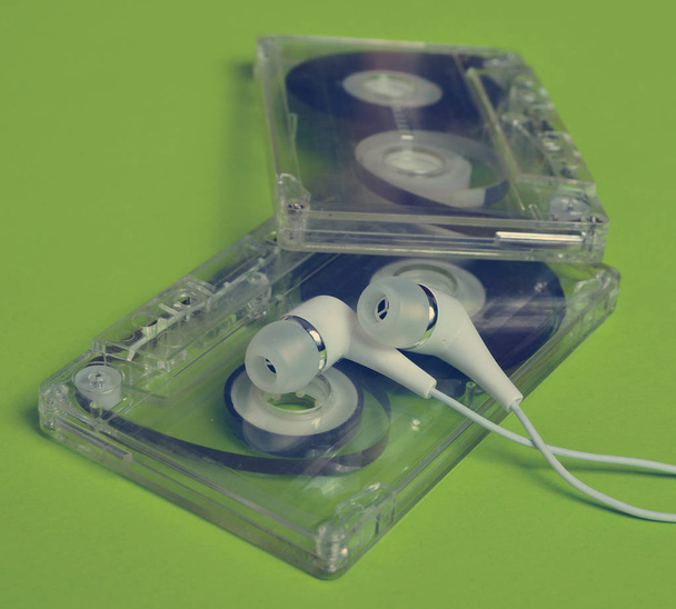 Ретро-технологія. Пластикова прозора аудіокасета та білі вакуумні навушники на яскраво-зеленому фоні. 80-ті роки
. - Фото, зображення
