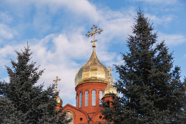 Ancienne église chrétienne en brique rouge à Kemerovo avec des dômes dorés et dorés contre un ciel bleu et des branches d'arbres. Concept de foi en Dieu, orthodoxie, prière
 - Photo, image