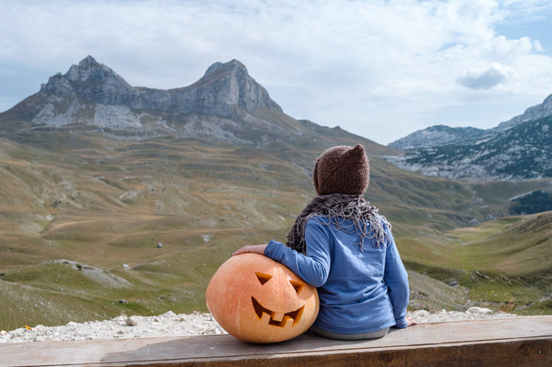 Back view of Cute boy in hat and Halloween Carved Pumpkin on the nature mountain background - Foto, imagen