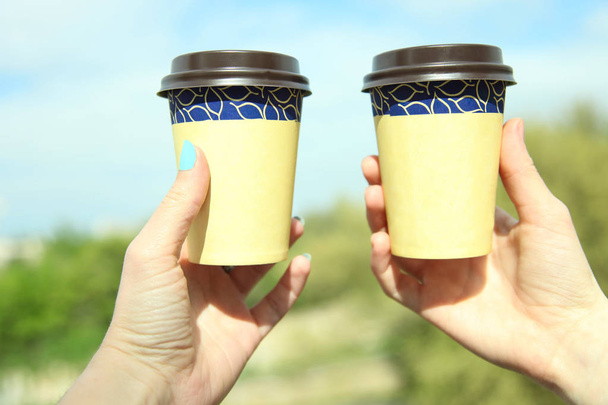 Dvě jednorázové sklenice s kávou v ruce na pozadí přírody. - Fotografie, Obrázek