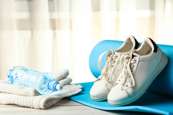 Gym mat, sneakers and water on wooden table front of window. Concept sport. - Photo, Image