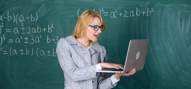 Educator smart clever lady with modern laptop searching information chalkboard background. Learn it easy way. Online schooling concept. Woman teacher wear eyeglasses holds laptop surfing internet - Photo, Image