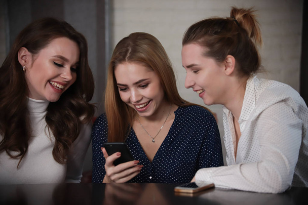 Jovens mulheres bonitas sentadas em um bar olhando no telefone, sorrindo
 - Foto, Imagem