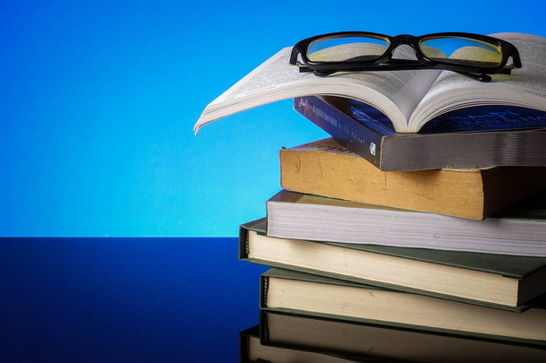 Eğitim kavramı ile yığın eski mavi bir arka plan üzerinde kitap ve okuma gözlükleri. - Fotoğraf, Görsel