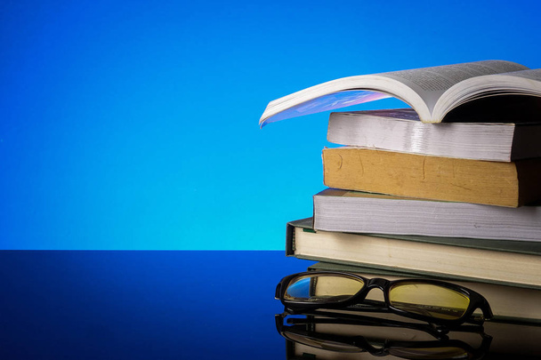 Bildungskonzept mit Stapel alter Bücher und Lesebrille auf blauem Hintergrund. - Foto, Bild
