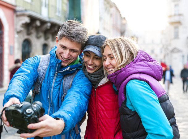 Ystävät ottavat selfien. Kolme ystävää kävelee kauniissa vanhassa kaupungissa. Matkustaa Euroopan kaupunkeihin. Kaksi naista ja mies kuvataan vanhojen rakennusten taustaa vasten.
. - Valokuva, kuva