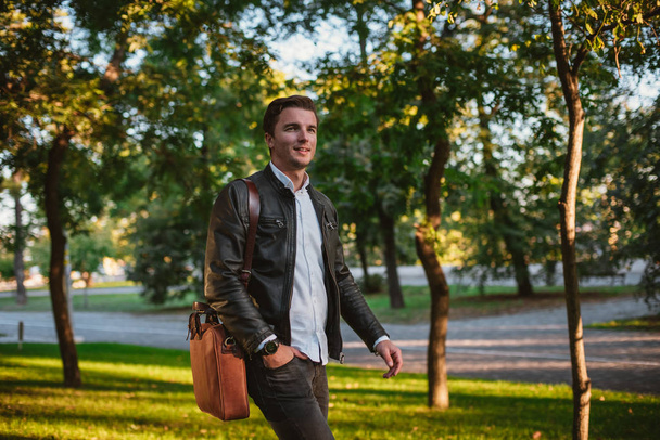 Young handsome man with bag walking in park during sunny day, autumn theme - Foto, immagini