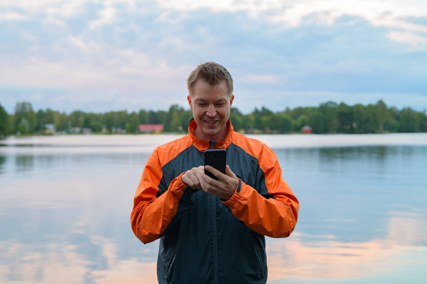 Счастливый молодой человек с телефоном на берегу озера
 - Фото, изображение