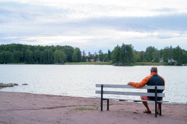 Hombre mayor sentado en el banco junto al lago
 - Foto, Imagen