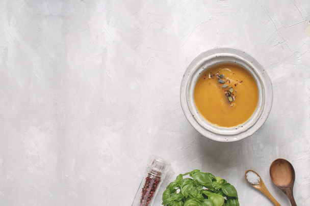 秋の食事フラット レイアウト - カボチャのスープ皿、ピンク胡椒、バジル、木製スプーン、平面図、灰色の背景コピー スペース. - 写真・画像