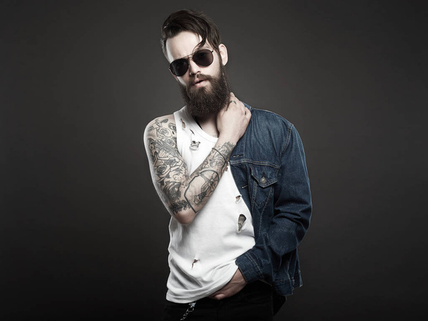 fashionable handsome man with tattoo and sunglasses. Hipster bearded Stylish boy in jeans and glasses - Photo, Image
