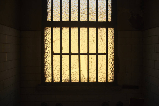 Window with bars of an abandoned building illuminated by the sun behind her is the central point of a dark room - Foto, Imagem