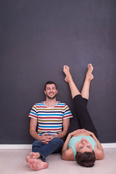 happy pregnant couple relaxing in front of black chalkboard on the floor at home - Photo, Image