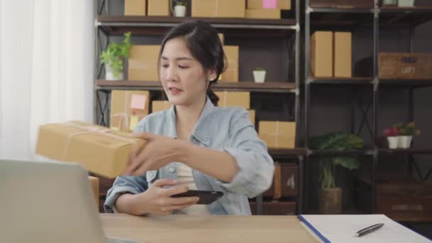 Kaunis älykäs aasialainen nuori yrittäjä liiketoiminnan nainen omistaja pk tarkistaa tuotteen varastossa scan qr koodi työskentelee kotona. Pienyrityksen omistaja kotona toimisto käsite
. - Materiaali, video