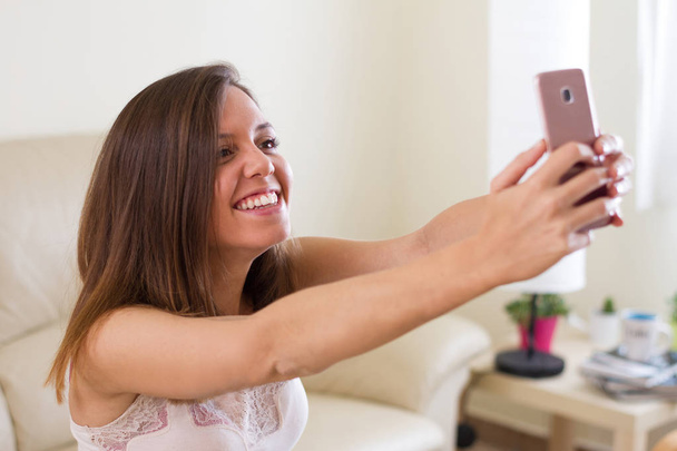 欧州ブルネットの少女、調達と幸せ、腕をモバイルの selfie を作る非常に幸せ、彼女の家のリビング ルームで素敵な笑顔 - 写真・画像