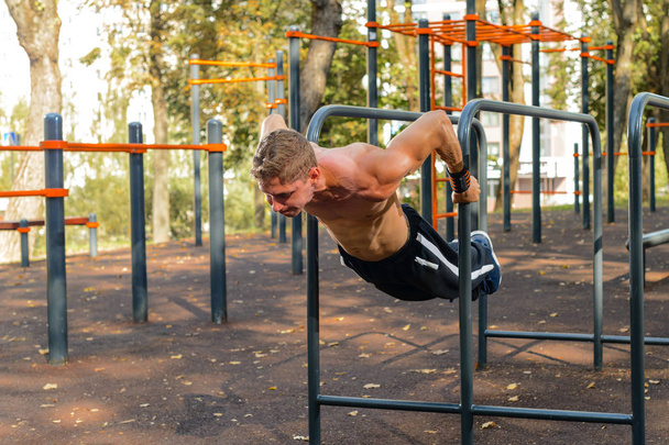 Athletic handsome man doing stand exercise on bar during calisthenics outdoors. Strength and endurance exercise. - Fotoğraf, Görsel