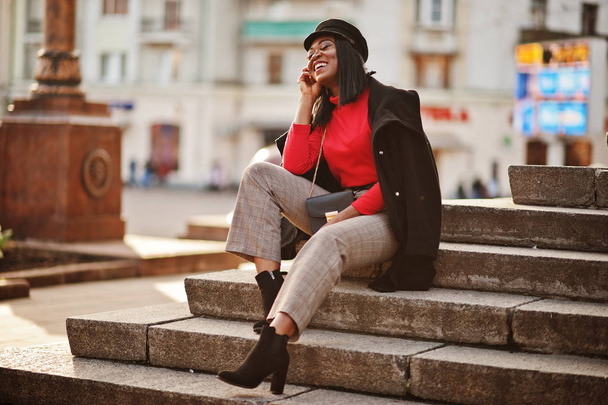 African american fashion girl in coat and newsboy cap posed at street. - Фото, зображення
