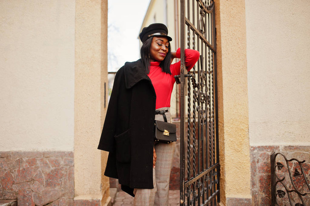 African american fashion girl in coat and newsboy cap posed at street. - Valokuva, kuva
