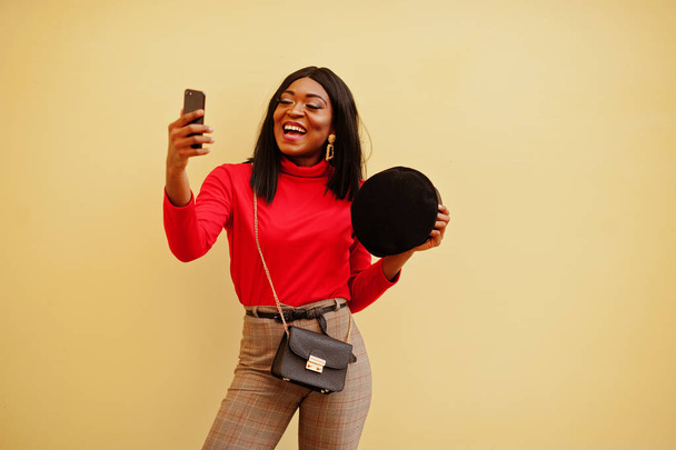 African american fashion girl with newsboy cap posed against yellow background with mobile phone. - Foto, imagen