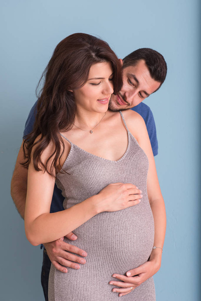 Portrait of a happy young couple,man holding his pregnant wife belly isolated over blue background - Foto, Imagen