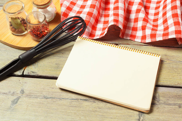 Blank sheet of opened notepad and kitchen utensils on  table with tablecloth, copy space - Foto, imagen